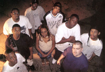 Scanned 1990s print of a nine-person crew photographed from above, everyone looking up into the camera.