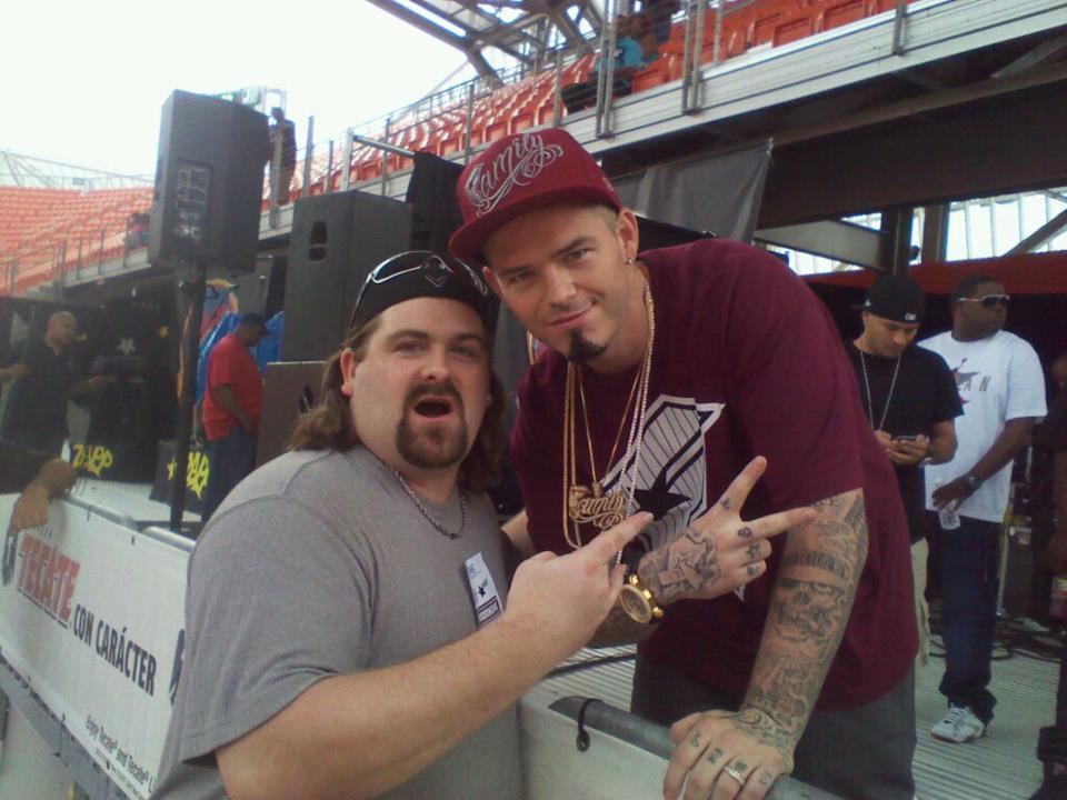 DJ Wrekk throwing a hand sign beside Houston rapper Paul Wall in the stands at a Houston stadium show.