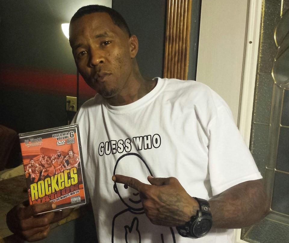 Macc Grace of the Screwed Up Click holding up a Rockets Nation Vol. 6 mix DVD by DJ Wrekk, wearing a 'Guess Who' t-shirt.