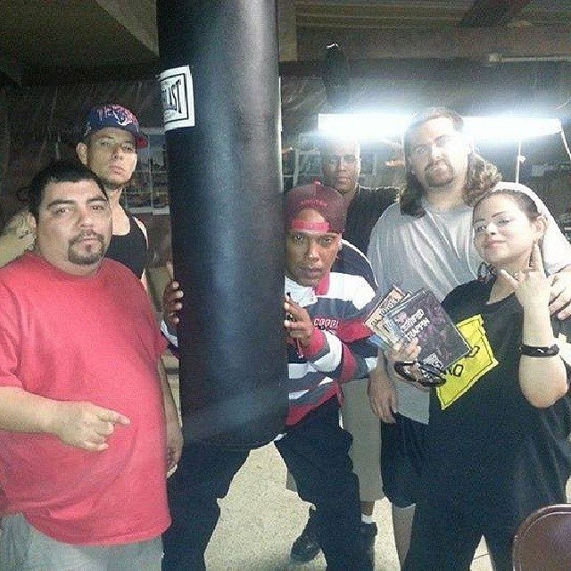 DJ Wrekk, Point Blank and four others posed around a punching bag in a garage, one holding mixtape CDs.
